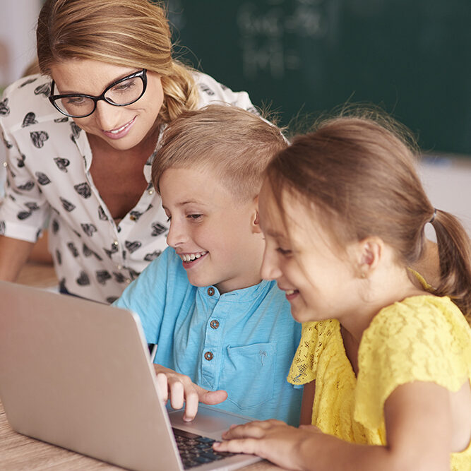 Teacher with students using laptop in classroom